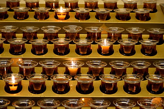 Rows of lit votive candles in a church prayer rack