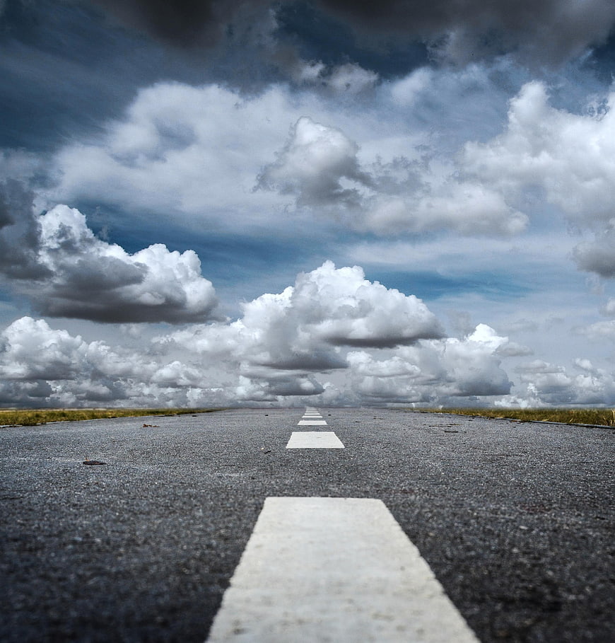 Low angle view of empty asphalt road with dramatic clouds