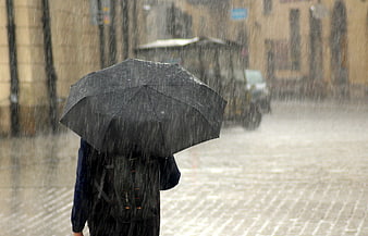 Person with black umbrella walking in heavy rain on city street