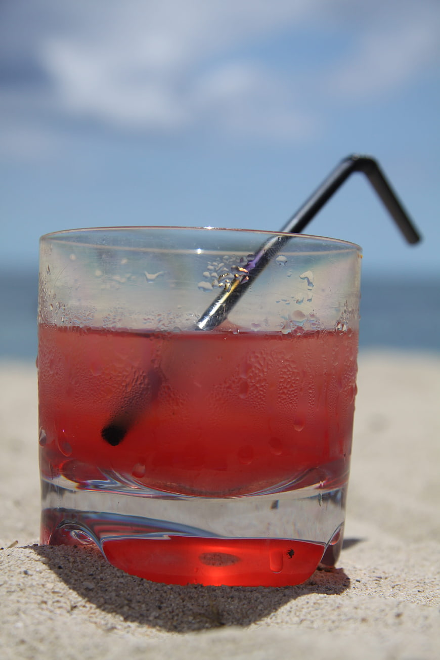 Cold red cocktail in glass on sandy beach with ocean background