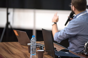 Laptop and water bottle on table with blurred speaker