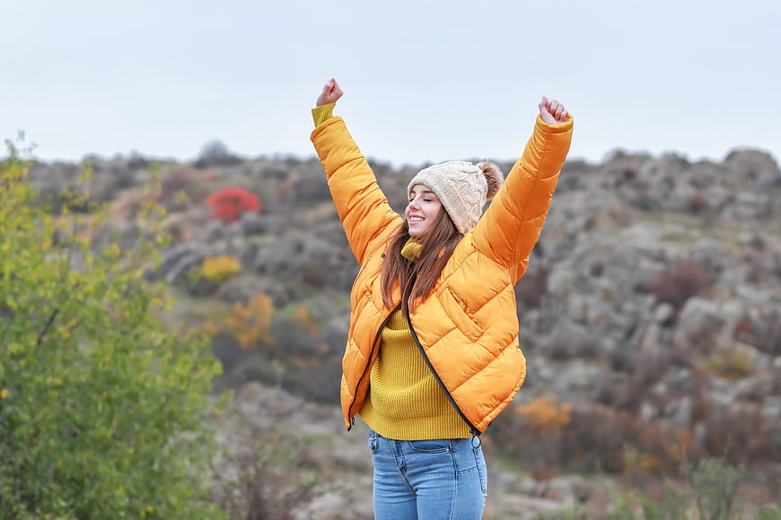 Happy woman in yellow jacket celebrating outdoors in autumn
