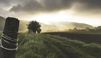 Dramatic Rural Landscape with Wooden Fence Post and Misty Hills