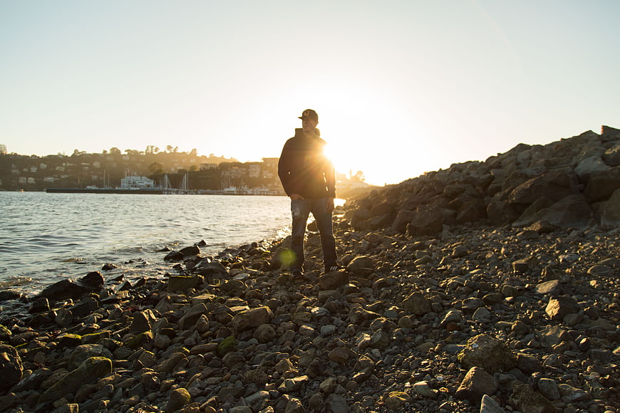 Man standing on rocky shore at sunset