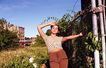 Young woman posing by chain-link fence in urban field