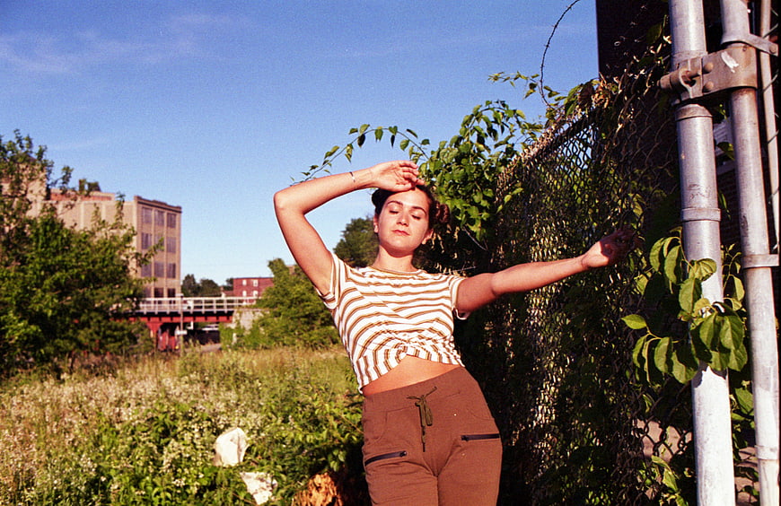 Young woman posing by chain-link fence in urban field