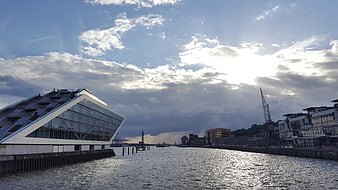 Modern angular building on riverbank with dramatic sky