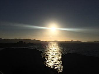 Sunset over ocean with silhouetted rocky coastline