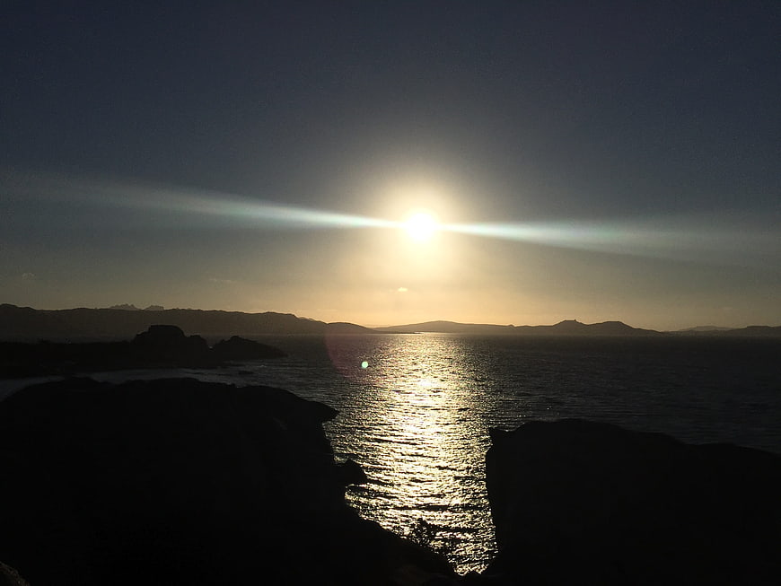 Sunset over ocean with silhouetted rocky coastline