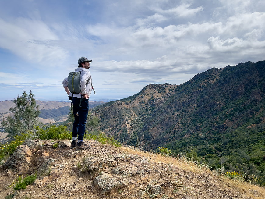 Hiker with Backpack Standing on Mountain Ridge Overlooking Valley