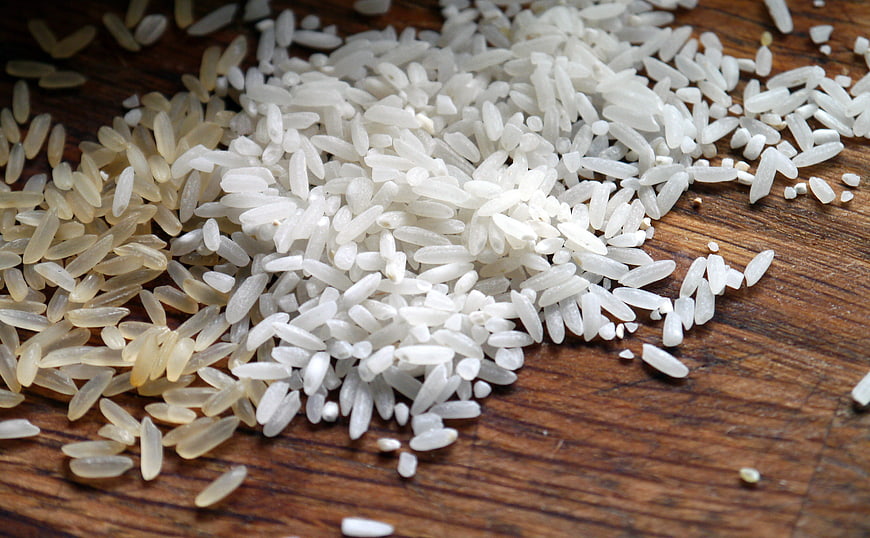 Raw white and brown rice grains on wooden surface