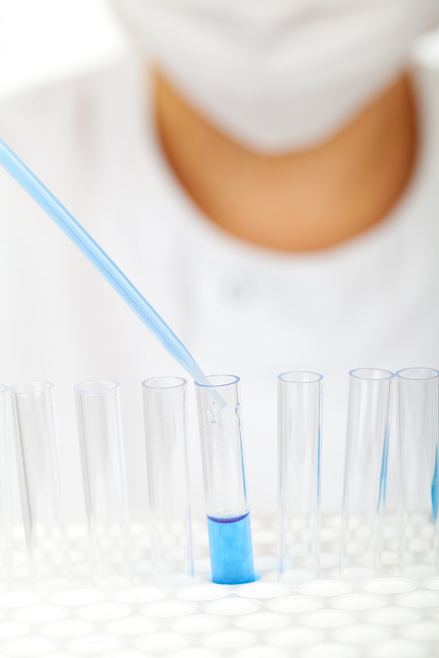 Scientist using pipette to fill test tube with blue liquid