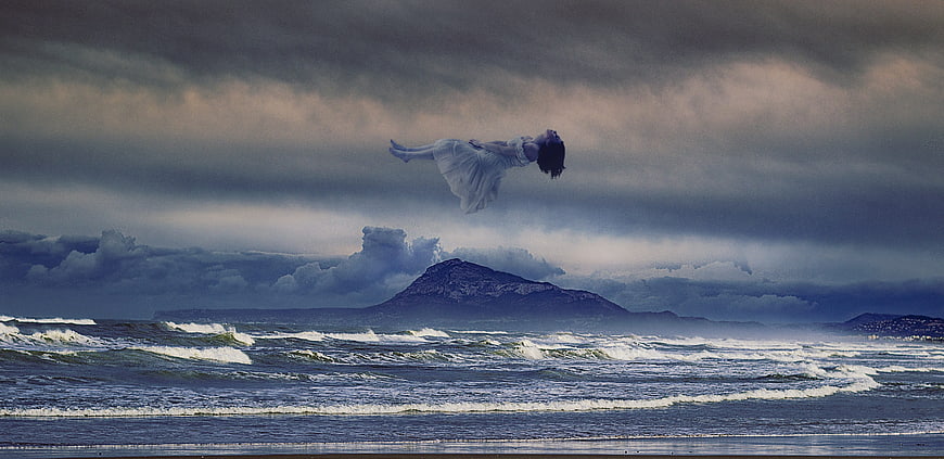 Woman floating in white dress over dramatic stormy ocean landscape