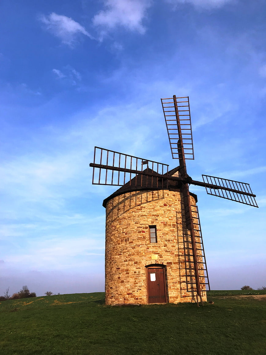 Historic stone windmill on grassy hill against blue sky