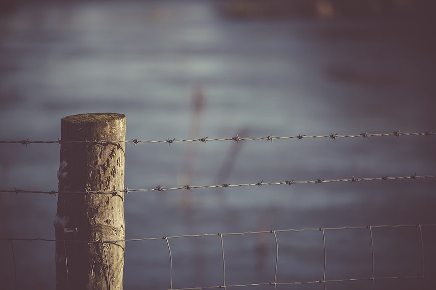 Rustic wooden fence post with barbed wire against blurred water background
