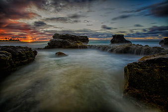 Dramatic Sunset Over Rocky Ocean Coastline with Long Exposure
