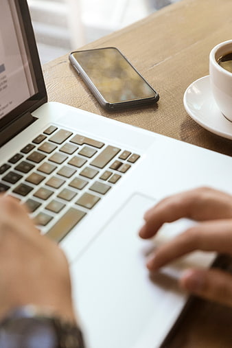 Close-up of hands typing on laptop with coffee and smartphone