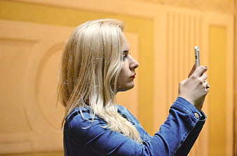 Blonde woman in denim jacket taking photo with smartphone