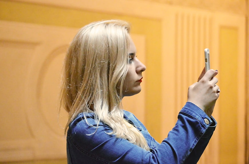 Blonde woman in denim jacket taking photo with smartphone
