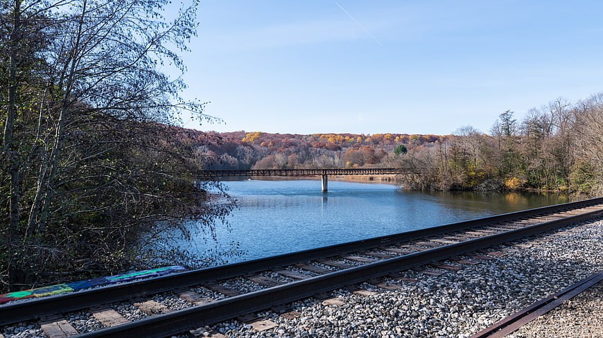 Railroad Tracks Along River with Autumn Forest and Bridge