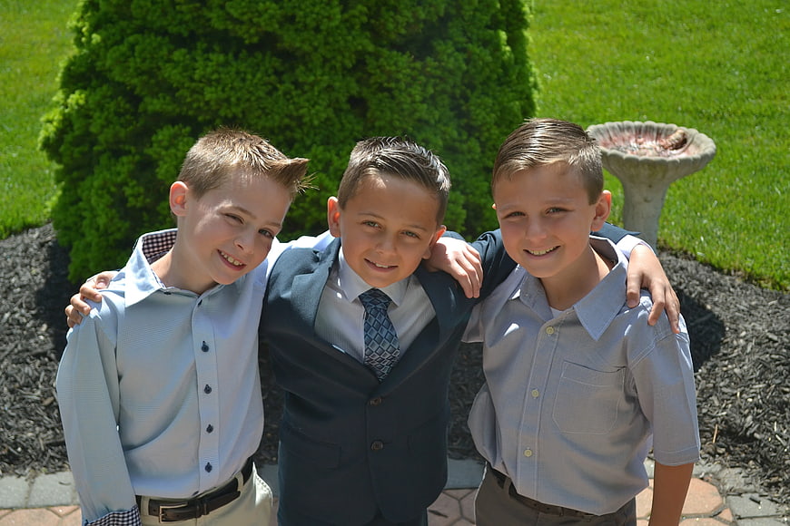 Three young boys in formal attire smiling outdoors