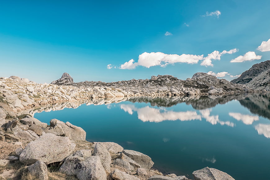 Serene Alpine Lake with Rocky Shore and Cloud Reflections