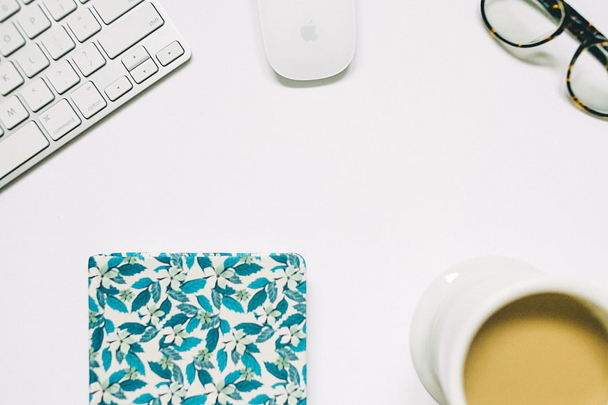 Minimalist white desk workspace with coffee and floral notebook