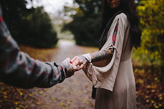 Couple holding hands with tattoos on autumn path