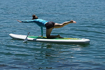 Woman doing yoga pose on paddleboard in blue water