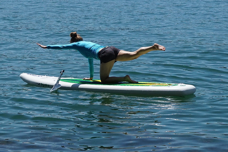 Woman doing yoga pose on paddleboard in blue water