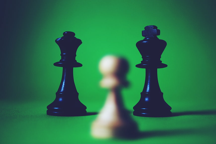 Black Chess Pieces Flanking Blurred White Pawn on Green Background