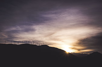 Silhouette of wind turbines on mountain ridge at sunset