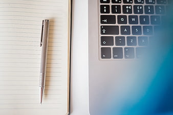 Grey Pen on Lined Notebook Beside Laptop Keyboard