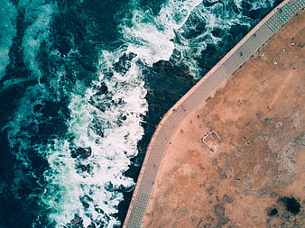 Aerial View of Turquoise Waves Crashing Against Sandy Beach Promenade