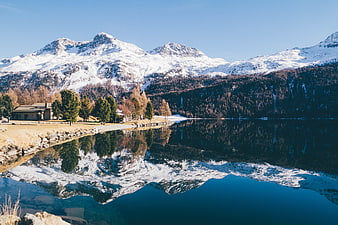 Snowy mountain landscape with lake reflection and cabin