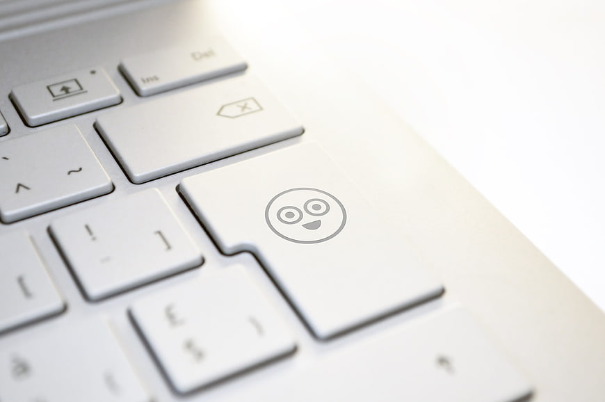 Close-up of a white laptop keyboard with a smiley face icon on the enter key