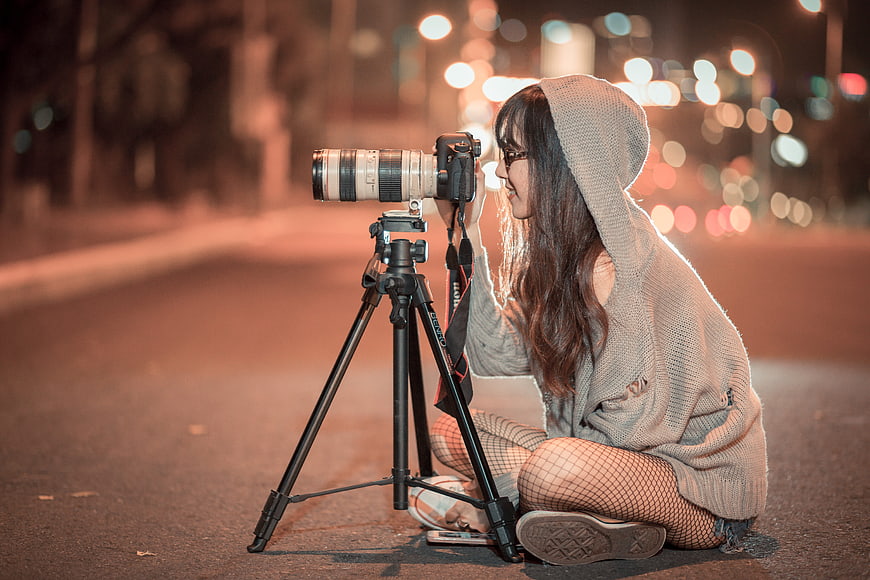 Young woman photographer adjusting camera on tripod at night