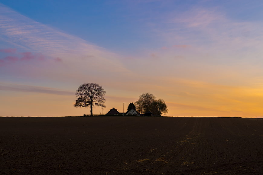 Silhouette of Farmhouse and Trees on Hill at Sunset