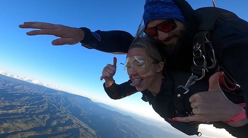 Tandem Skydiving Couple Freefalling Over Mountainous Landscape