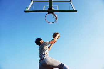Young Man Dunking Basketball Against Blue Sky