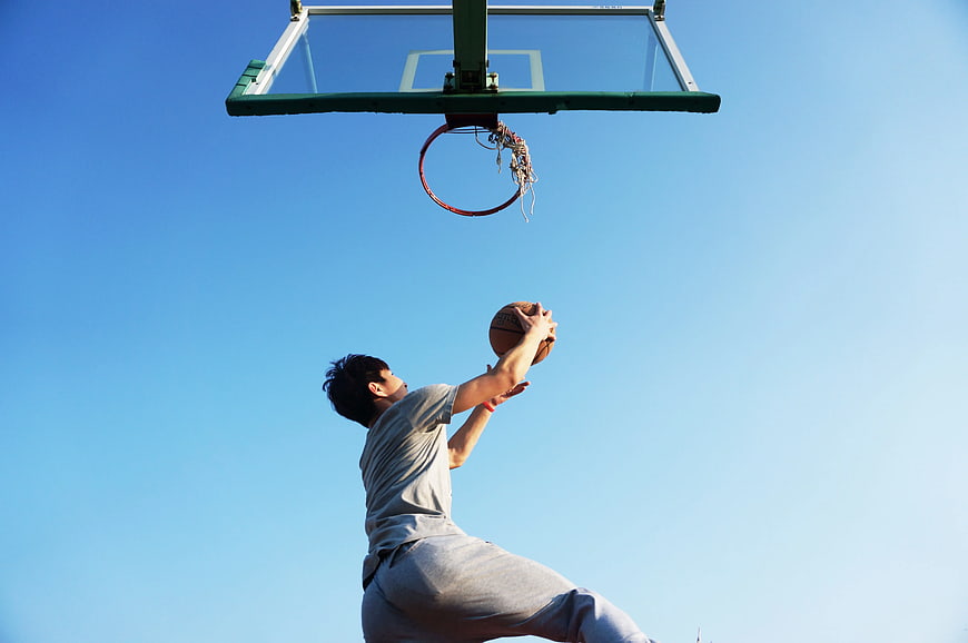 Young Man Dunking Basketball Against Blue Sky