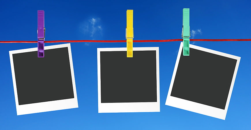 Three empty polaroid frames hanging on a red clothesline against a blue sky