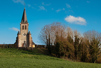 Historic stone church on a grassy hill under blue sky