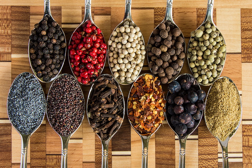 Assorted Spices And Herbs In Silver Spoons On Wooden Board