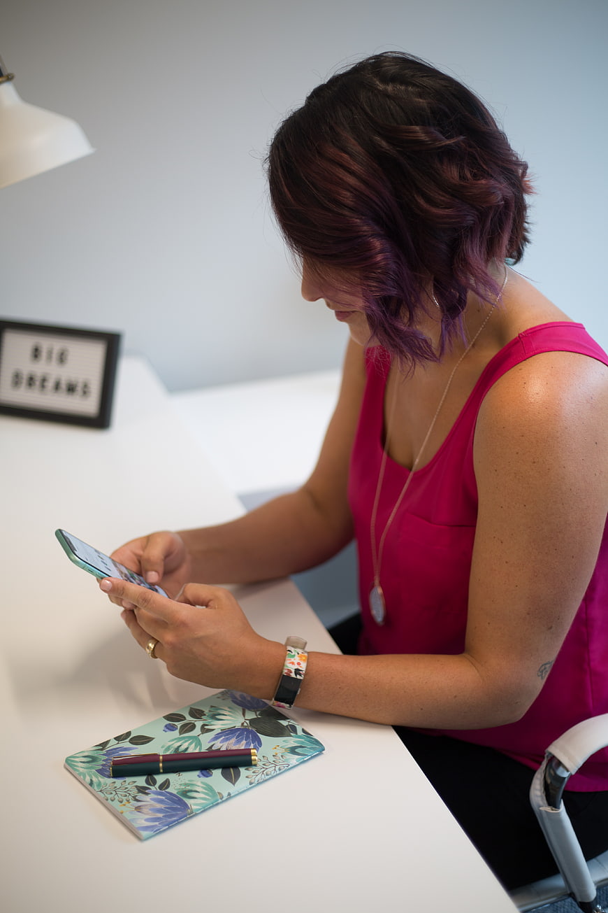 Woman with purple hair using smartphone at white desk