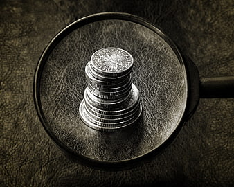 Stack of coins under magnifying glass on dark leather background