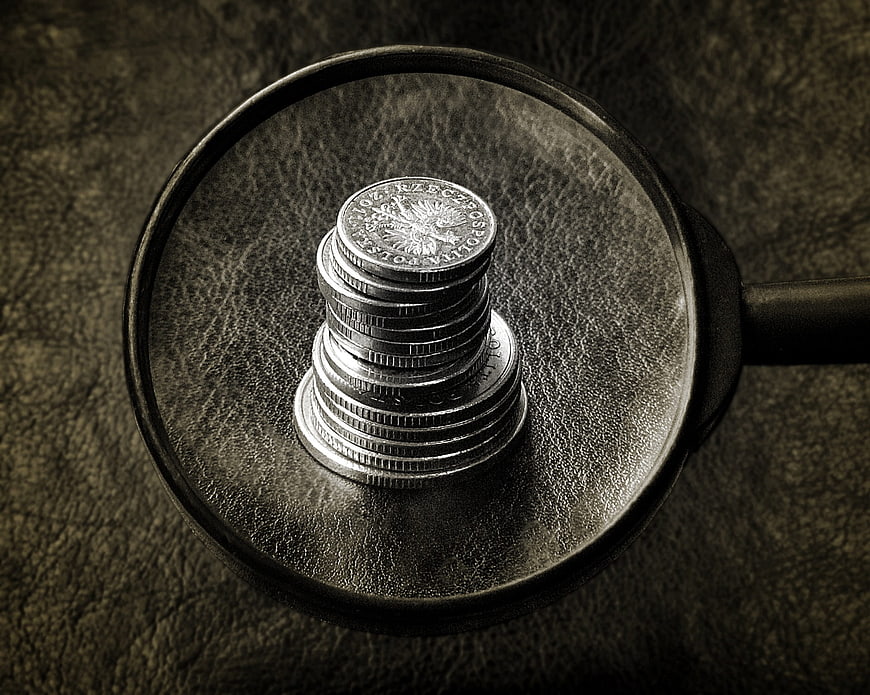 Stack of coins under magnifying glass on dark leather background