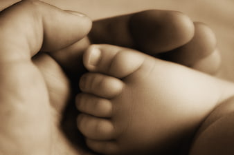 Close-up of adult hand holding tiny baby foot in sepia tone