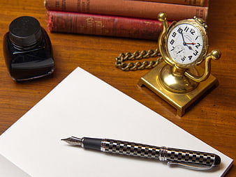 Vintage fountain pen, pocket watch, and ink on wooden desk