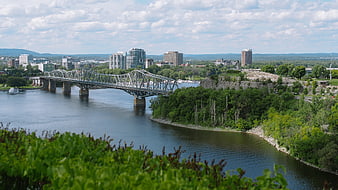 Steel truss bridge over river with city skyline and green cliffs